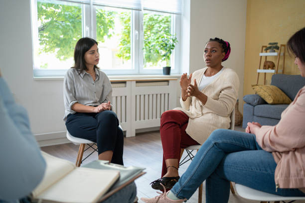 While sitting in a circle, multiracial group of women and men, having group therapy, led bu psychotherapist